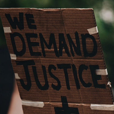 Stock image from UNSPLASH of person holding up a placard saying "Wed demand justice + change"