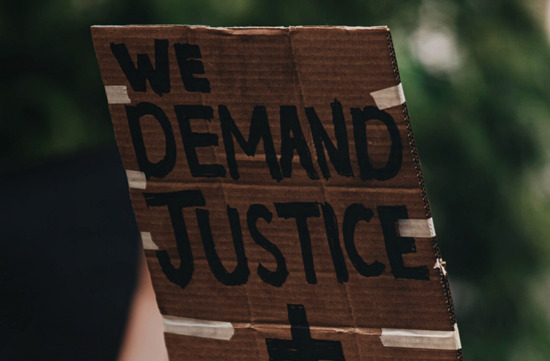 Stock image from UNSPLASH of person holding up a placard saying "Wed demand justice + change"