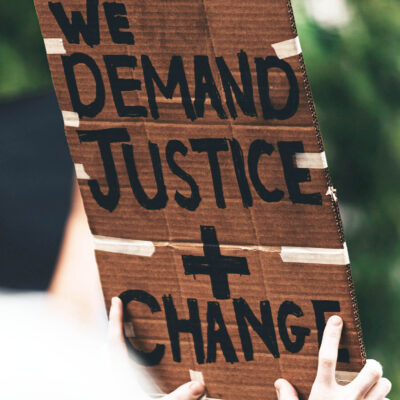 Stock image from UNSPLASH of person holding placard saying "Demand justice + change"
